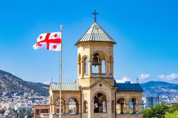 Beautiful view to Georgian Flag on the background chapel on site to Sameba Cathedral Tsminda in Tbilisi Holy Trinity . Biggest church Orthodox in Caucasus Georgia region in a sanny day.
