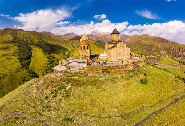 Pandangan atas yang indah dari drone ke Tsminda Sameba atau Gereja Tritunggal Kudus Dekat Desa Gergeti di Georgia dan gunung tinggi Kazbek, pegunungan Kaukasus. Tempat umum untuk dikunjungi . — Stok Foto