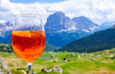 Renkli İtalyan çayırları ve Dolomites Alpleri dağlarının arka planında geleneksel İtalyan alkollü içkisi Aperol Spritz'in manzarası. köy St. Cristina di Val Gardena Bolzano Seceda, İtalya.