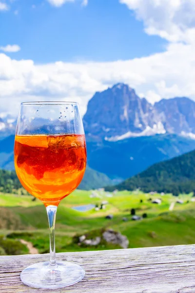 View of the traditional Italian alcoholic drink Aperol Spritz on the background of colorful Italian meadows and the Dolomites Alps mountains. village St. Cristina di Val Gardena Bolzano Seceda, Italy. — Stock Photo, Image