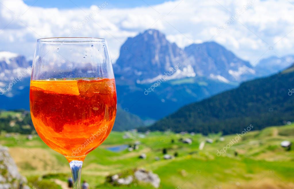 View of the traditional Italian alcoholic drink Aperol Spritz on the background of colorful Italian meadows and the Dolomites Alps mountains. village St. Cristina di Val Gardena Bolzano Seceda, Italy.