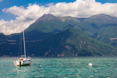 Como Gölü'ndeki Varenna köyünde limana demirlemiş yelkenlinin manzarası. Arka plan alpler dağlar, ağaçlar ve su üzerinde Manzara manzara. Lecco Milano Eyaleti. İtalyan bölgesi Lombardiya, İtalya Avrupa