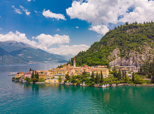 Beautifull aerial panoramic view from the drone to Varenna - famous old Italy town on bank of Como lake. High top view to Water landscape with green hills, mountains and city in sunny summer day.