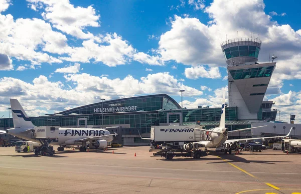 Helsinki Havalimanı Finlandiya 26.07.2019: Finnair havayolu teknisyenleri bagajı konteynerden uçağın kuyruğundaki bölmeye yüklerler. İki Airbus pistte duruyor ve uçuş bekliyor