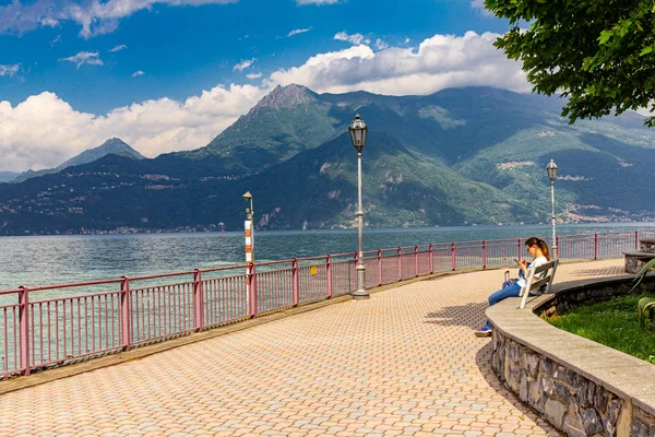 Rıhtımda oturan ve Varenna civarında manzaraları keşfetmek Avrupalı kız. Yaz güneşli bir günde yüksek dağların ve sahil gölü Como'nun güzel manzarası. İtalya, Avrupa. — Stok fotoğraf