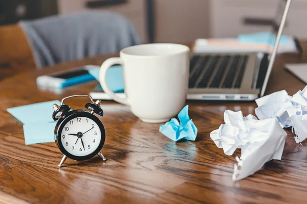 Clock on wood table at office workplace background with laptop, coffee cup and smart phone