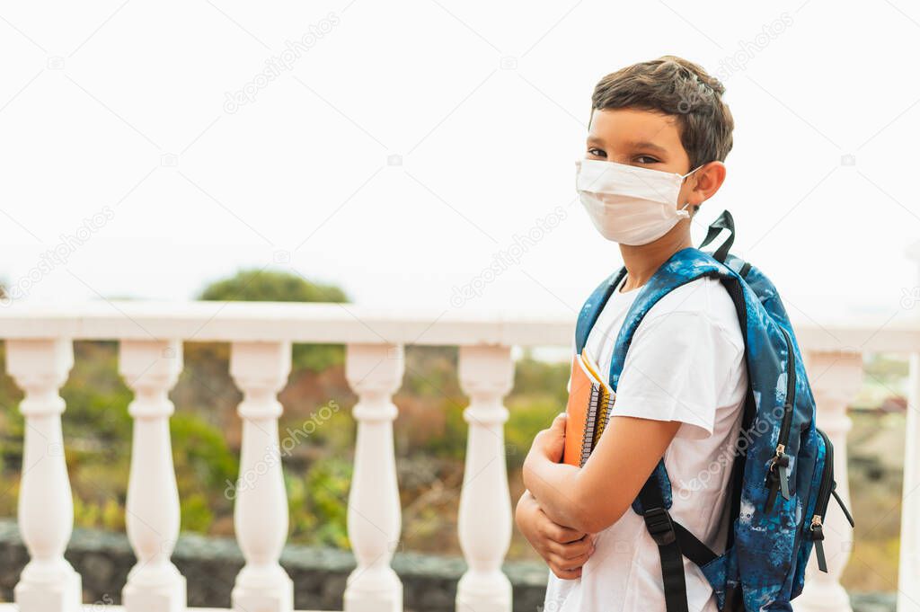 COVID-19 coronavirus concept. School with a medical mask to protect the health of the influenza virus. Student girl with backpack and books - outdoor portrait. The boy goes back to school.