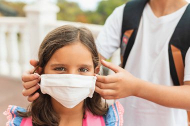 Erkek kardeşi kız kardeşine steril tıbbi maske takıyor. Çocuk, yüz maskesi takıyor, karantinada virüs, salgın ve salgın hastalıklardan korunuyor..