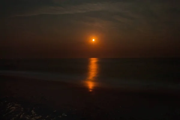 Night seascape with a red moon and a moonlight path