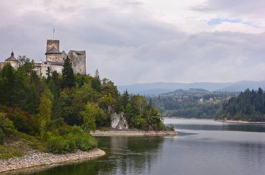 Nedzice, Polonya ve Avrupa 'daki antik Dunajec kalesi. Bulutlu bir günde gölün üstündeki tepede eski bir şatonun manzarası.