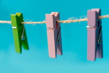 Mavi arkaplan fotoğrafında izole edilmiş bir ipte üç tane çok renkli ahşap mandal.