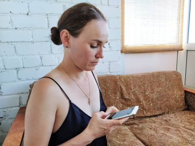 Kadın kanepede oturuyor, telefonu kullanıyor ve düşünüyor.