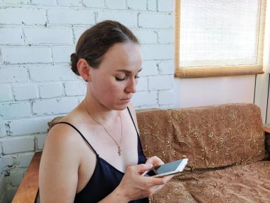 Kadın kanepede oturuyor, telefonu kullanıyor ve düşünüyor.