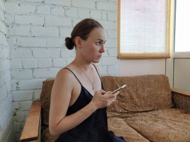 Kadın kanepede oturuyor, telefonu kullanıyor ve gelecekteki randevusunu düşünüyor, arkadaşlarıyla buluşuyor.