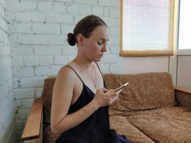 Kadın kanepede oturuyor, telefonu kullanıyor ve gelecekteki randevusunu düşünüyor, arkadaşlarıyla buluşuyor.