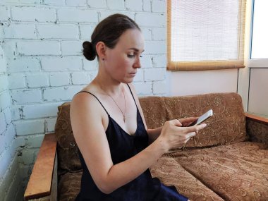 Kadın kanepede oturuyor, telefonu kullanıyor ve gelecekteki randevusunu düşünüyor, arkadaşlarıyla buluşuyor.