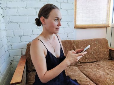 Kadın kanepede oturuyor, telefonu kullanıyor ve gelecekteki randevusunu düşünüyor, arkadaşlarıyla buluşuyor.