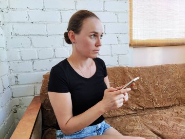 Milenyum kadını kanepede oturuyor ve telefonu sakin bir ifadeyle kullanıyor.