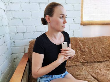 Milenyum kadını koltukta oturur, telefonu göğsüne bastırır ve uzaklığa bakar.