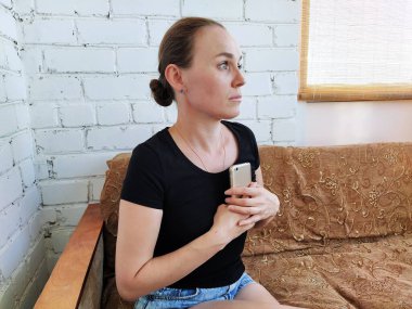 Milenyum kadını koltukta oturur, telefonu göğsüne bastırır ve uzaklığa bakar.