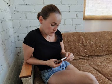 Milenyum kadını kanepede oturuyor ve telefonu sakin bir ifadeyle kullanıyor.