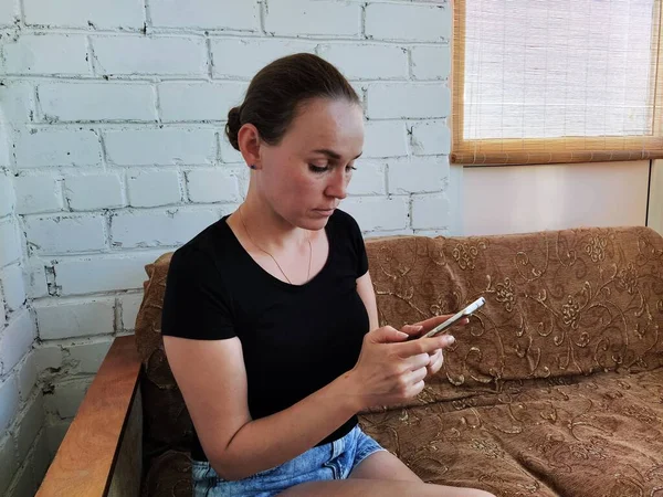 Milenyum kadını kanepede oturuyor ve telefonu sakin bir ifadeyle kullanıyor.