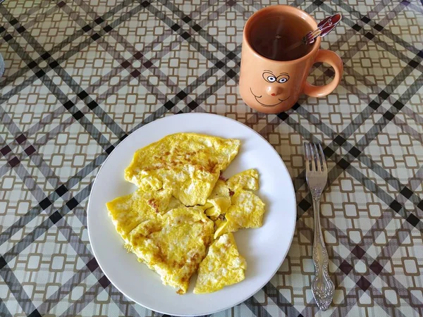 Bir tabak omlet ve üzerinde gülen surat olan bir kupa çay.