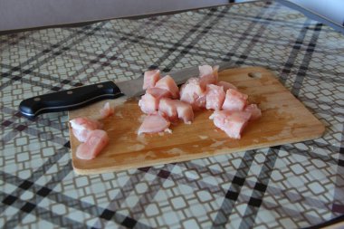 Kesme tahtasının üzerinde bıçakla kesilmiş tavuk göğsü parçaları.