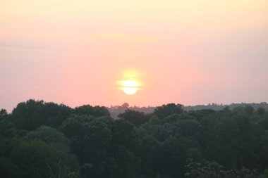 Tepelerin ve ağaçların üzerinde batan güneş