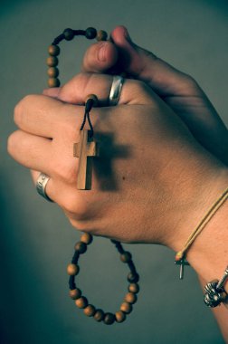 Manos de mujer caucsica rezando el rosario de cruz y cuentas de madera