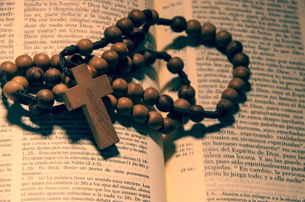 Rosario de Cruz y cuentas de madera sobre biblia abierta en pasaje en Castellano 