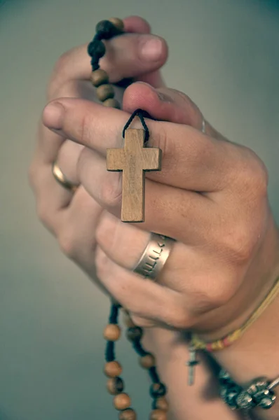 Manos de mujer caucsica rezando el rosario, rosario de Cruz y cuentas de madera