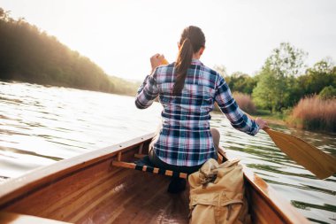 Kız kanosu. Günbatımında sandalda kürek çeken gezgin kadının arka görüntüsü.