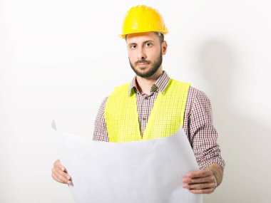 Beyaz arka planda duran sarı kasklı ve yelekli inşaat işçisi.