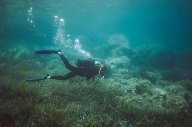 Kayalık zemini olan bir adam suyun altına dalıyor.