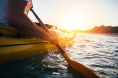 Güneş doğarken deniz suyunda kayak yapan bir adam.