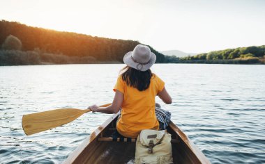 Gün batımı gölünde şapka kürek çeken bir kızın arka görüntüsü.