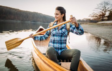Gezgin kız gölde kano yapmayı sever. Sırt çantalı genç bir kadın kanoda kürek çekiyor, boşluğu kopyala