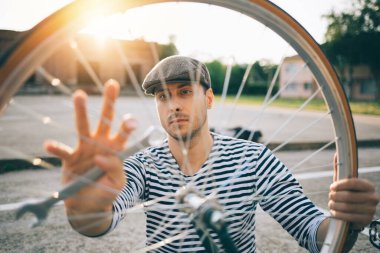 Dışarıda bisikleti tamir eden gri şapkalı çocuk.