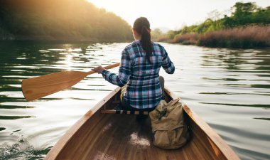 Tahta kanoya kürek çekiyorum. Günbatımı gölünde kano süren seyahat kızlarının arka görüntüsü. Kano, kano, açık hava.
