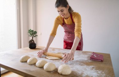 Ekmek hamurunu mutfak masasında oklavayla yoğuran kadın. Ev yapımı pişirme.