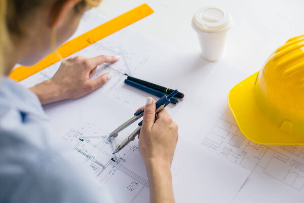 Woman architect draws a plan, design, geometric shapes by pencil on large sheet of paper at office desk.