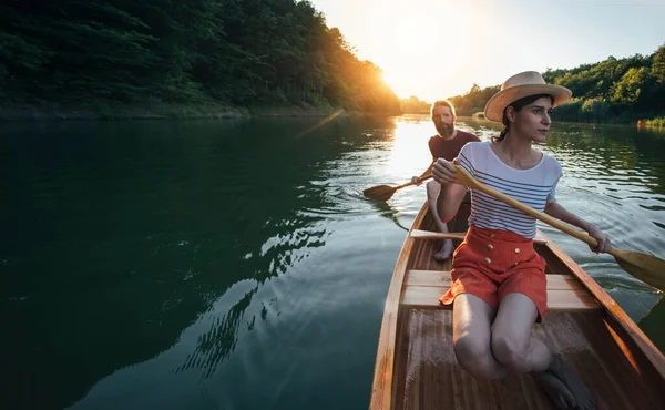 Young couple sailing on canoe on river sunset