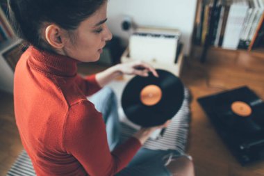 Hippi kızın elinde en sevdiği plak plağı var. Düşük açılı bir kız evde müzik dinlemekten hoşlanıyor.