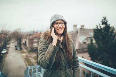 Akıllı telefondan konuşan genç bir kadın. Gülümseyen milenyum kızı dışarıda cep telefonuyla konuşuyor..
