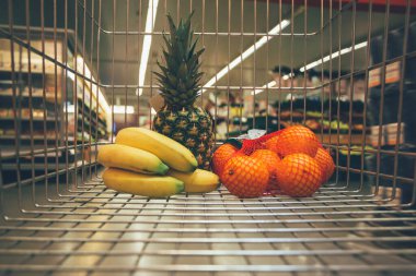 Süpermarkette meyveli alışveriş arabası. Market arabasında muz, ananas ve portakal meyvesi..