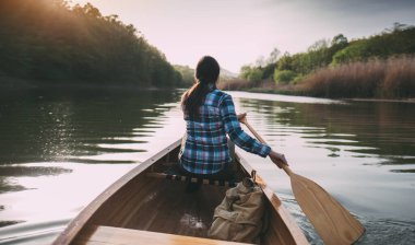 Kız kanosu. Günbatımında sandalda kürek çeken gezgin kadının arka görüntüsü.