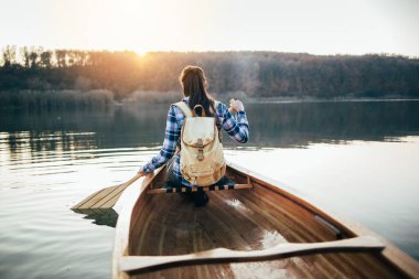 Sırt çantalı bir kadın kanoyla gezmekten zevk alıyor. Gün batımı gölünde kanoda kürek çeken bir kız.