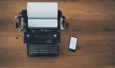 Ahşap arka planda akıllı telefonu olan eski bir daktilo. İş, teknoloji gelişimi konsepti. Boşluğu kopyala