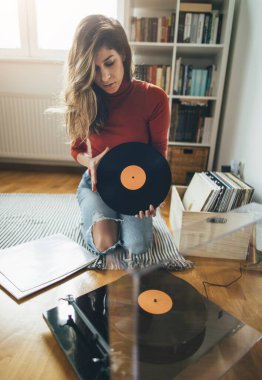 Hippi kızın elinde en sevdiği plak plağı var. Düşük açılı bir kız evde müzik dinlemekten hoşlanıyor.